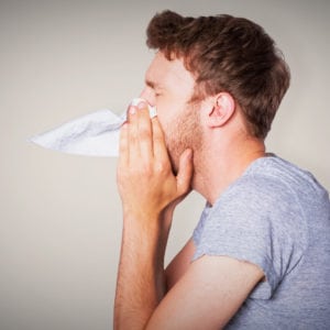 man blowing nose into tissue