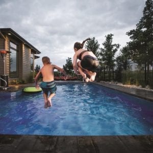 Two kids jumping into an in-ground pool.