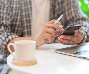 Man holding a mobile phone with cup of coffee and laptop